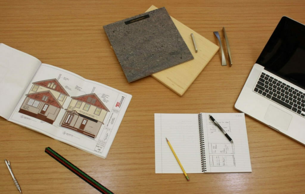 Architectural plans, a laptop, design materials, and sketchbooks arranged on a wooden table.