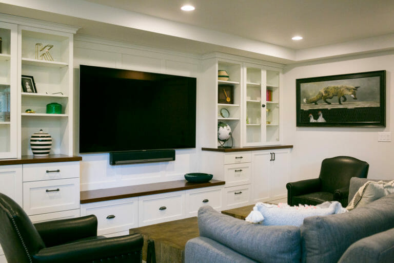 Modern living room featuring a large TV, white cabinetry, decorative items, and a black armchair.