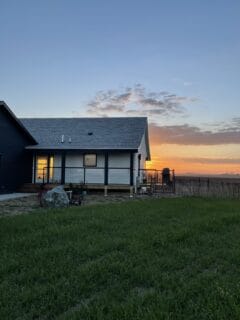 A cozy house with a blue exterior at sunset, surrounded by green grass and a wooden fence in the background.