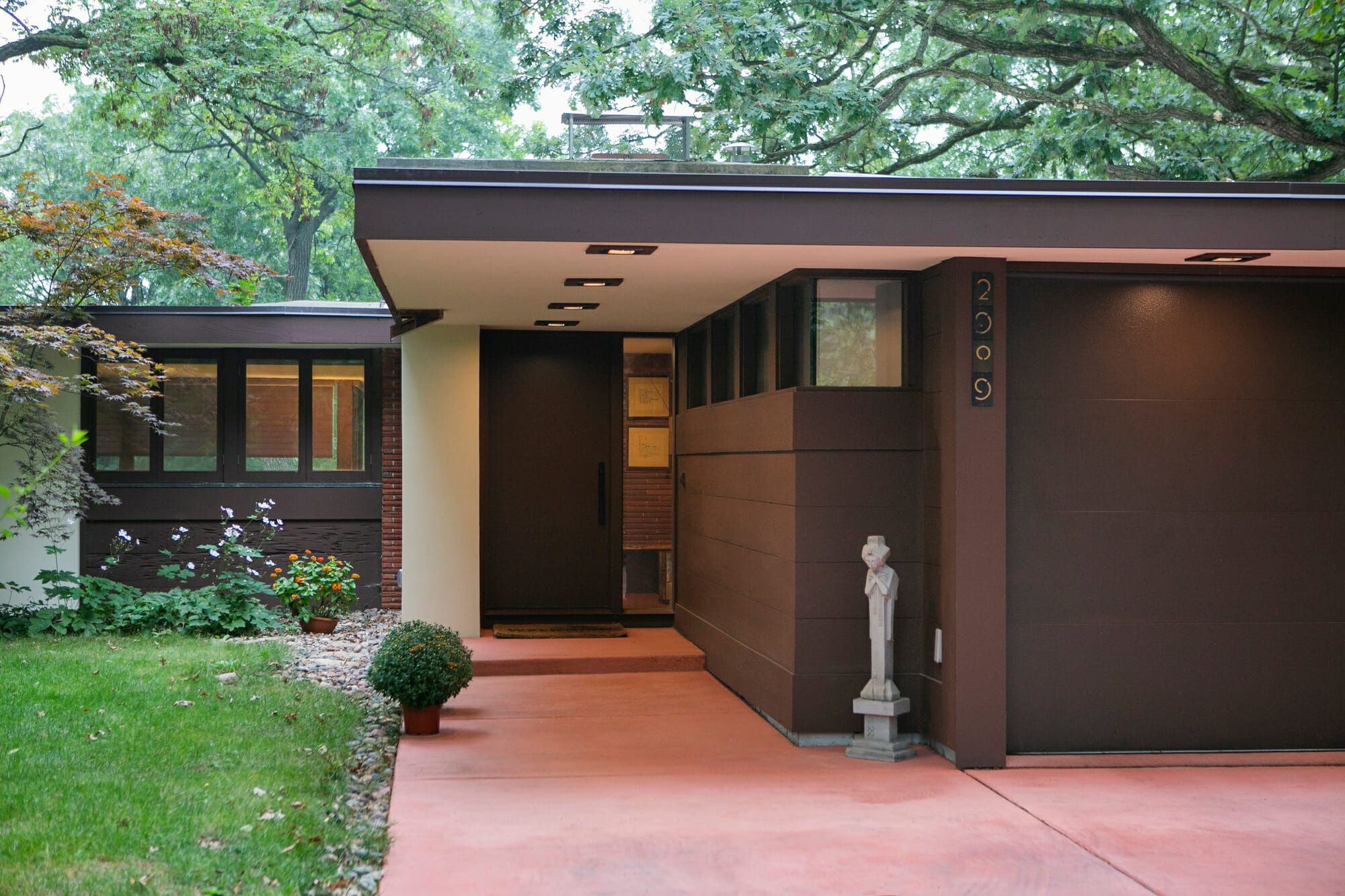 Modern home entrance with dark wood accents, landscaped garden, and a decorative statue beside the door.