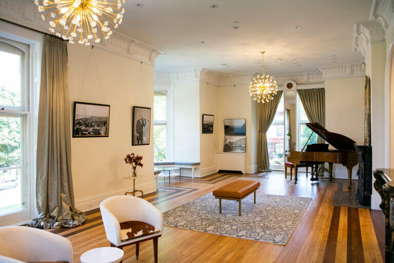 Elegant room featuring a grand piano, modern lighting, and framed photographs, with wooden floors and plush seating.