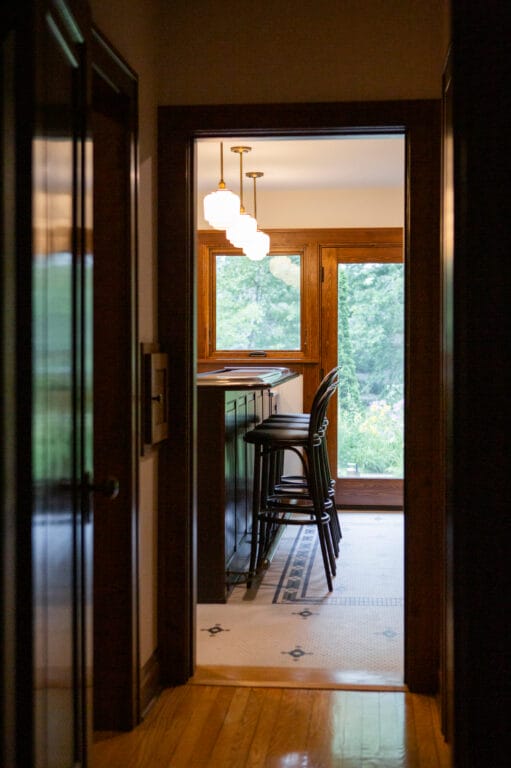 View through a hallway into a cozy bar area with wooden accents, bar stools, and large windows overlooking greenery.