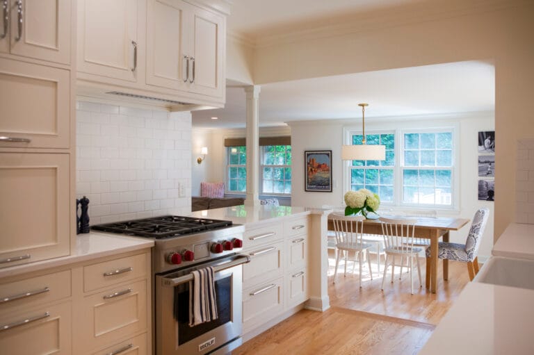 Bright, modern kitchen with white cabinetry, a gas stove, and a dining area featuring a wooden table and floral centerpiece.