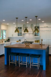 Modern kitchen featuring a blue island, wooden countertop, gold pendant lights, and sleek white cabinetry.