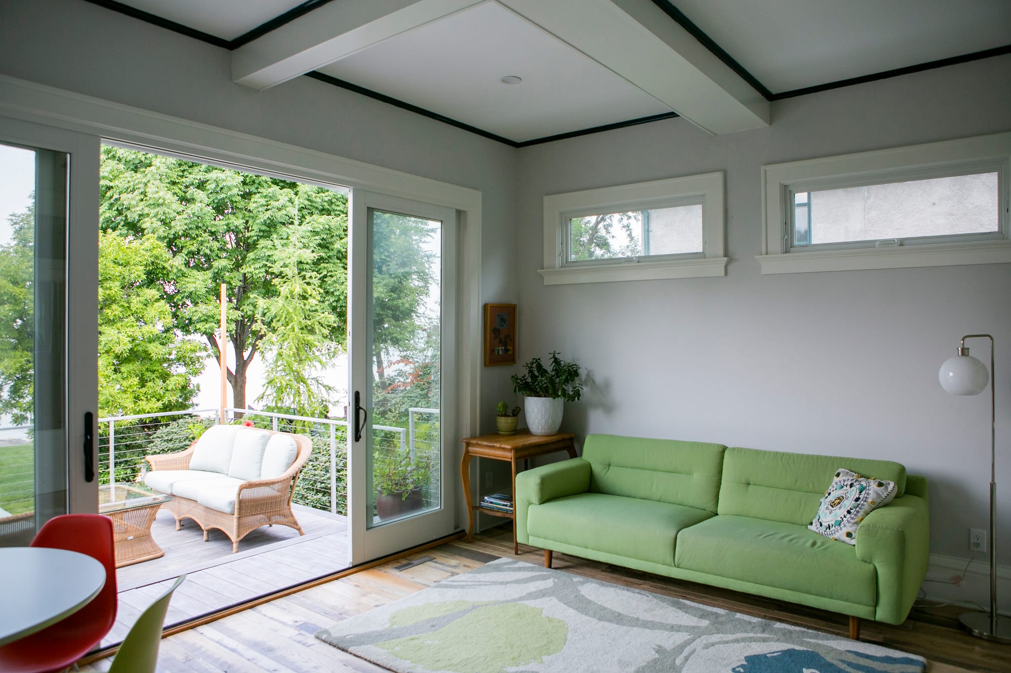 Bright living room featuring a green sofa, large glass doors, and a view of lush trees outside.