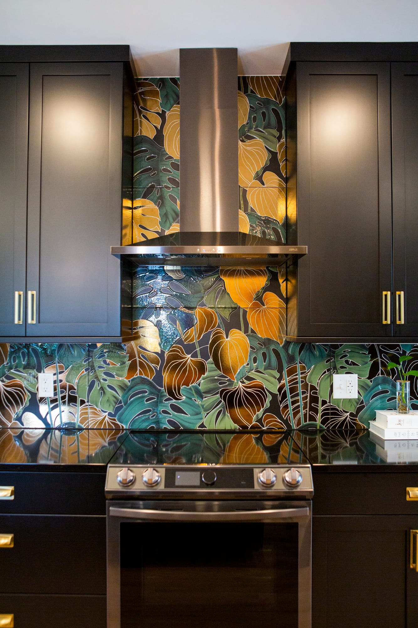 Stylish kitchen featuring a vibrant leaf-patterned backsplash and modern stainless steel range hood against dark cabinetry.