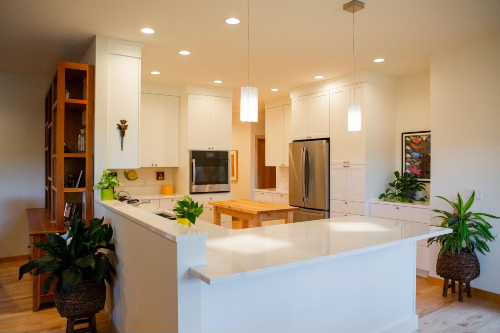 Bright, modern kitchen featuring white cabinetry, stainless steel appliances, a wooden island, and potted plants.