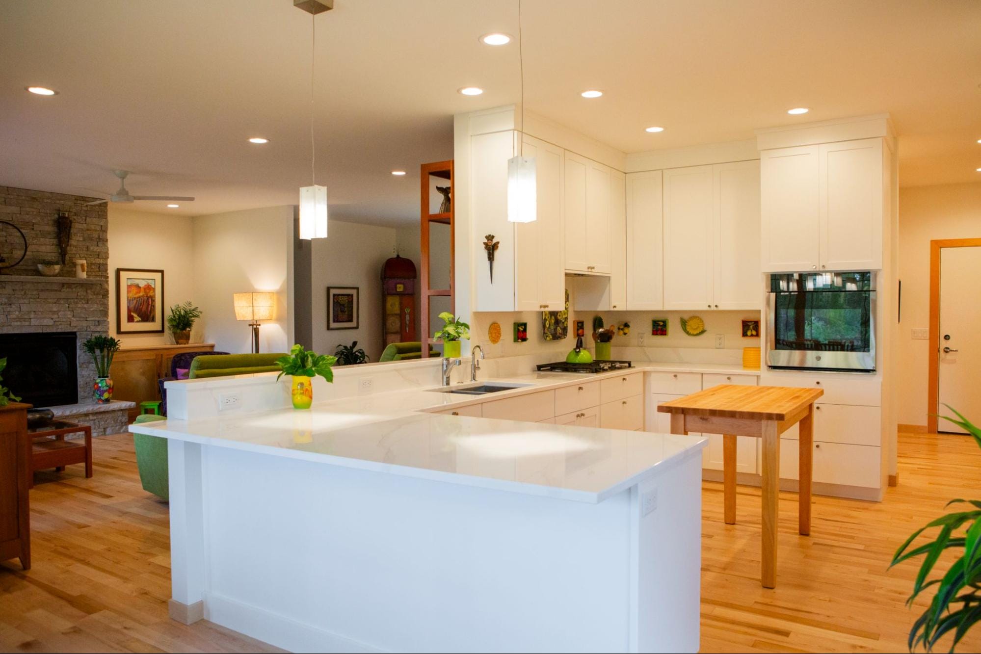 Bright, modern kitchen featuring white cabinets, a wooden island, and a cozy living area with a stone fireplace.