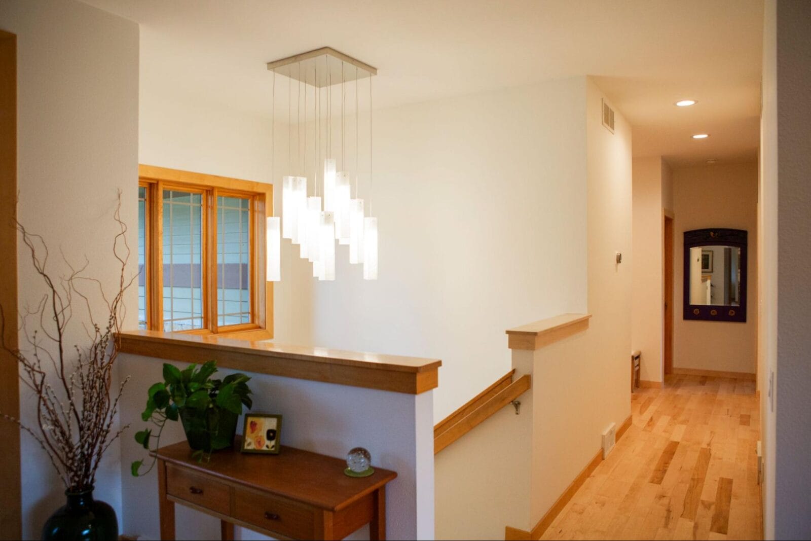 Bright hallway featuring modern pendant lighting, wooden accents, a potted plant, and a mirror at the end.