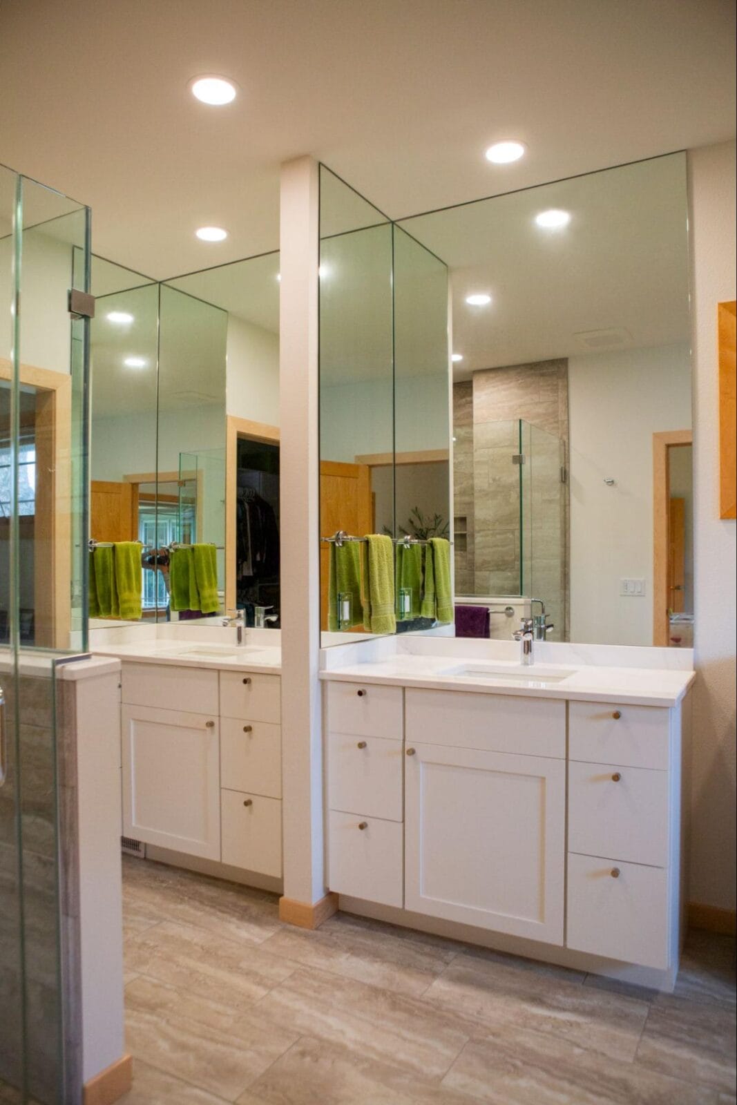 Modern bathroom featuring dual vanities, large mirrors, glass shower, and vibrant green towels on display.