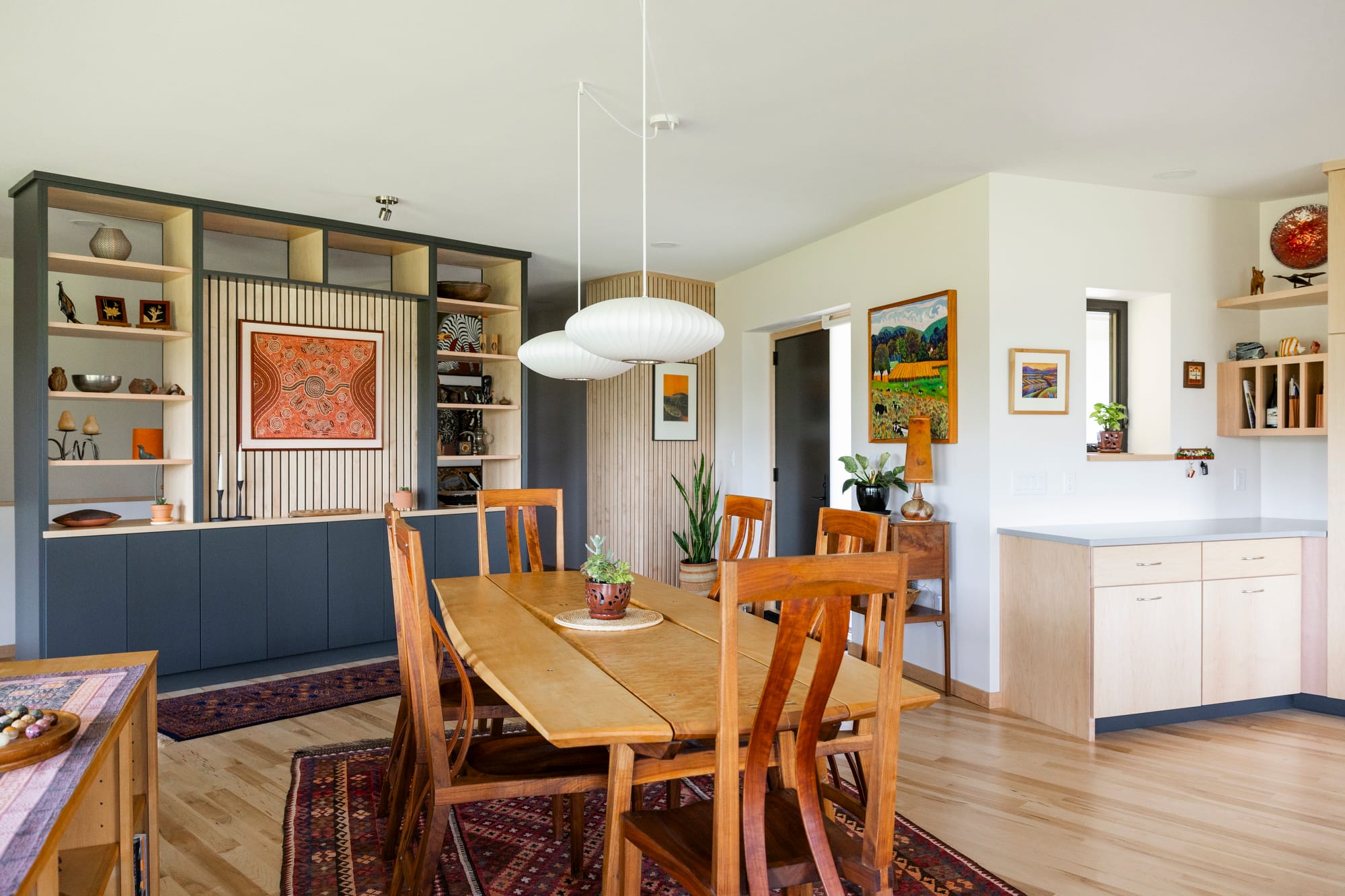 Modern dining area featuring a wooden table, stylish chairs, and a decorative shelving unit with art and plants.