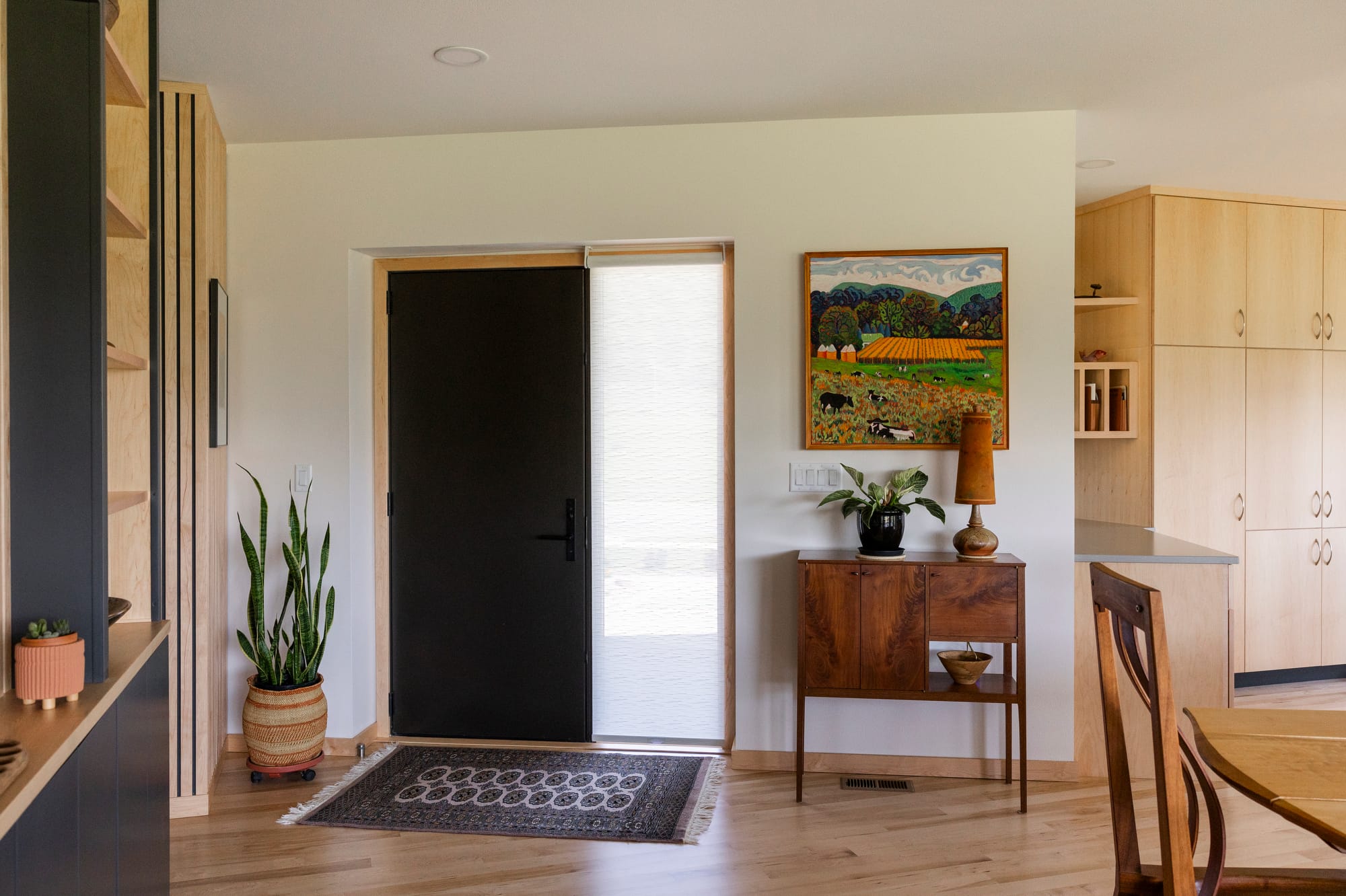 Modern entryway featuring a black door, wooden furniture, a colorful painting, and indoor plants.