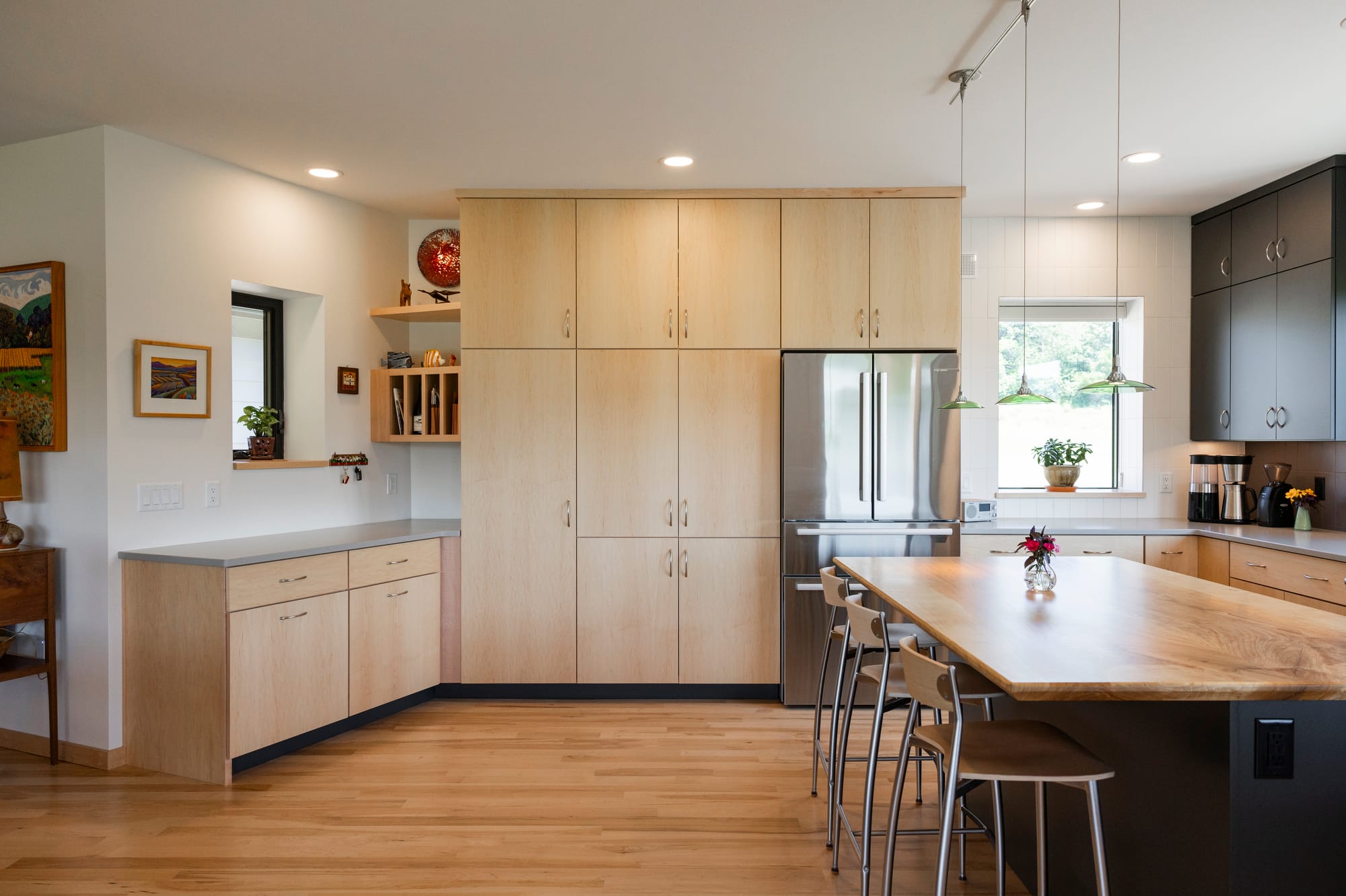 Modern kitchen featuring light wood cabinetry, stainless steel appliances, and a large wooden island with seating.