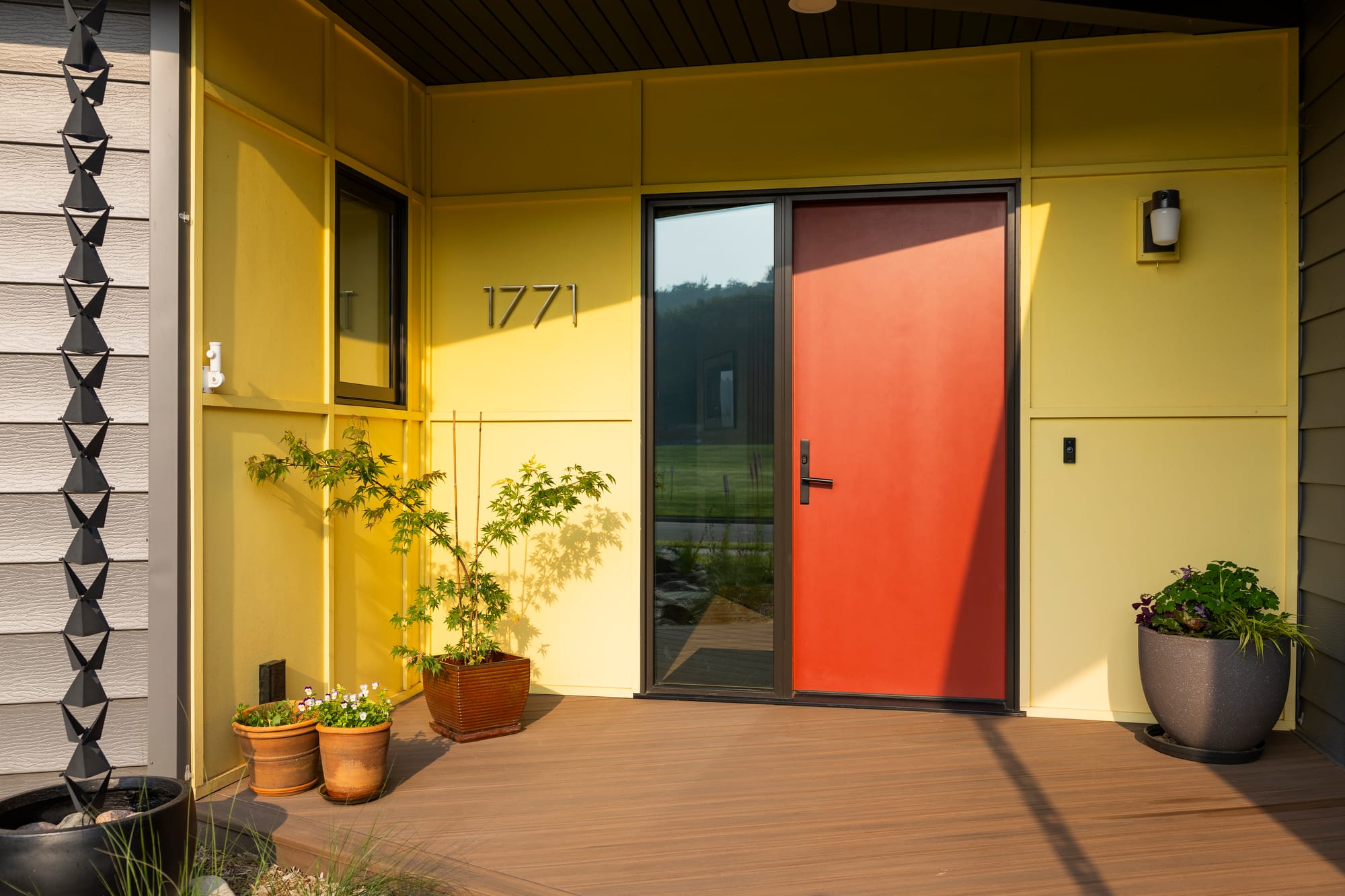 Vibrant yellow entryway featuring a bold red door, potted plants, and the house number 1771 displayed prominently.