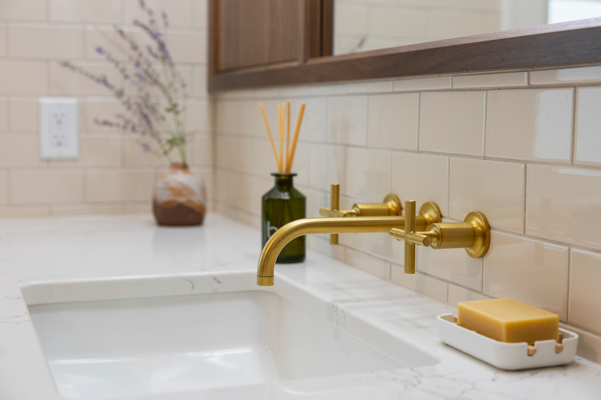 Gold wall-mounted faucet over a white sink with soap and diffuser.