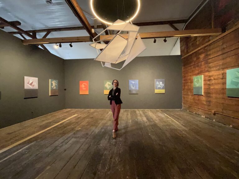 Woman in art gallery with abstract paintings and sculpture.