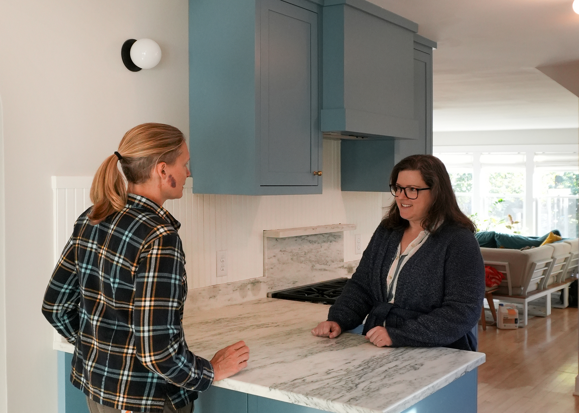 Two people standing in a kitchen and speaking to each other across a marble countertop.